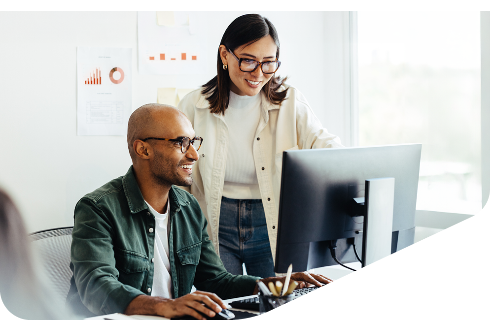 Zwei Personen arbeiten gemeinsam am Computer, lächelnd, mit Datenvisualisierungen an der Wand im Hintergrund. Zwei Personen arbeiten gemeinsam am Computer, lächelnd, mit Datenvisualisierungen an der Wand im Hintergrund.